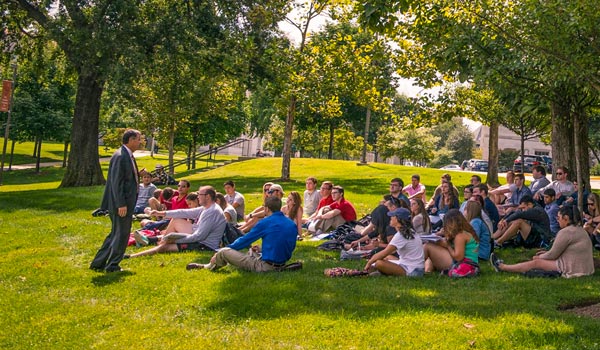Students sitting on grass listening to an outdoor lecture